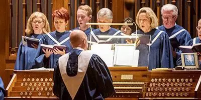 Choir standing behind organ while organist plays