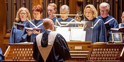 Choir standing behind organ while organist plays
